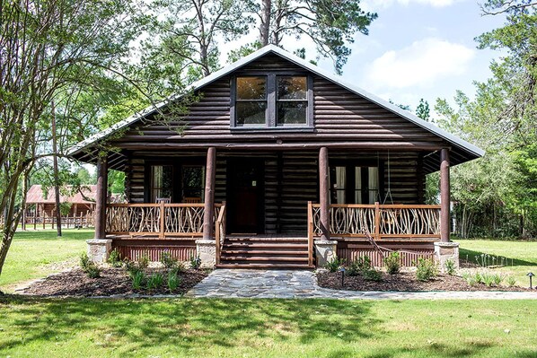 A rustic log cabin with a porch, stone steps, and a small garden. - Fully Restored Cabin with Private Hut-Tub in Livingston, Texas (Livingston)