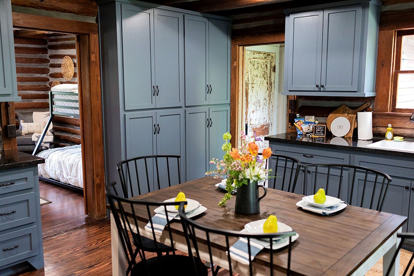 A log cabin interior with a dining area, kitchen, and a bed.