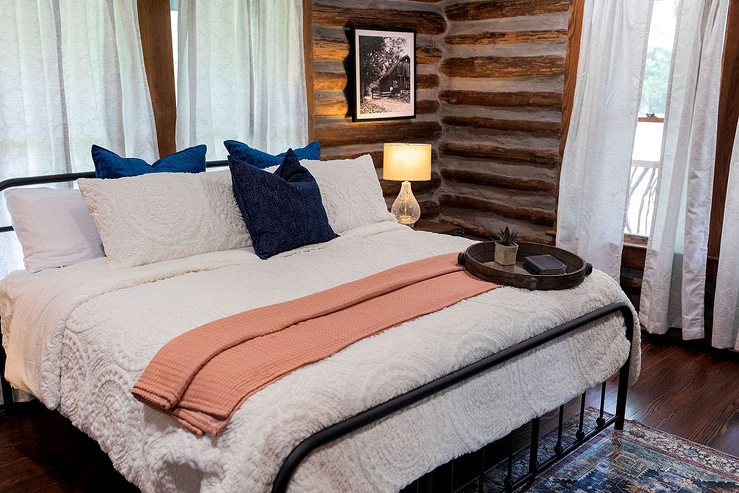 Ein Bett mit weißer und pfirsichfarbener Tagesdecke, einem schwarzen Metallgestell und blauen Kissen.