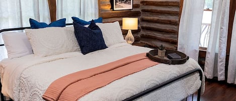 Una cama con una manta blanca y melocotón, estructura metálica negra y almohadas azules.