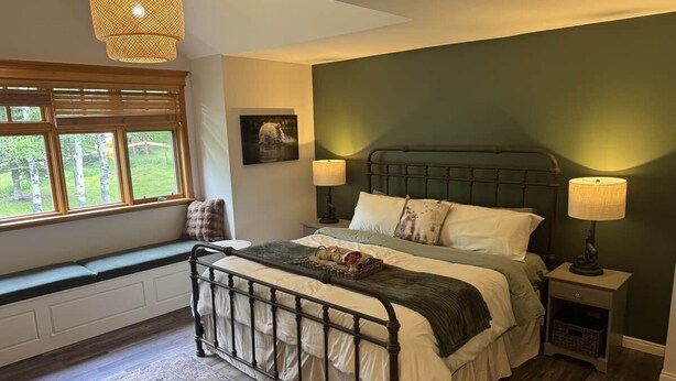 Een slaapkamer met een bed, bedlampen, een vensterbank en uitzicht op groen.