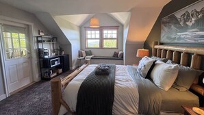Une chambre à coucher avec un lit, un banc, une télévision et une fenêtre donnant sur un beau paysage.
