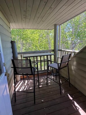 Een overdekte veranda met een tafel en stoelen, houten vloer en uitzicht op bomen.