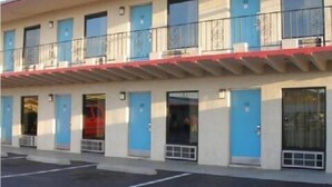 Un motel con varias habitaciones, cada una con puerta y ventana, y un estacionamiento al frente.