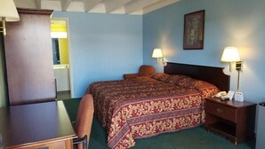 Una habitación de hotel con una cama, una silla, un escritorio, una mesita de noche y una lámpara.