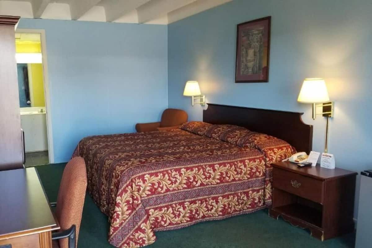 Et hotelværelse med seng, stol, skrivebord, natbord og lampe.