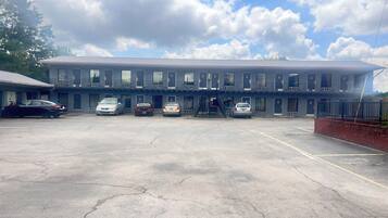 A motel with a row of rooms, a parking lot, and a clear sky.