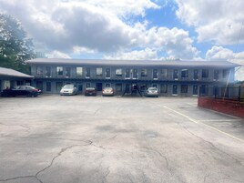 A motel with a row of rooms, a parking lot, and a clear sky.