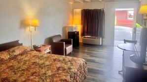 Una habitación de hotel con cama, escritorio, silla, televisor y aire acondicionado.