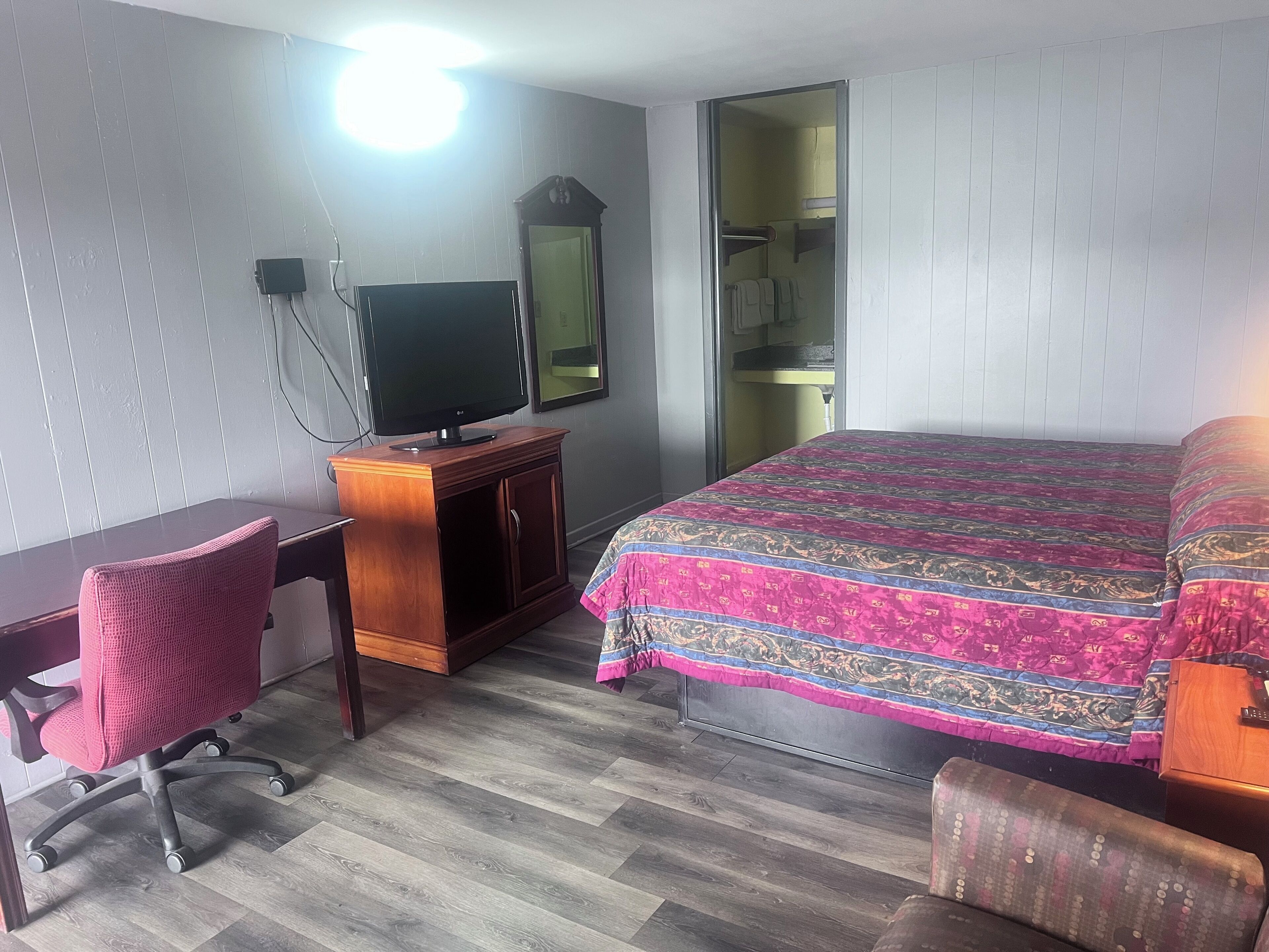 Habitación de hotel con escritorio de madera, televisión, cama con cubrecama estampado, silla y armario.