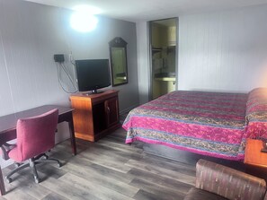 A hotel room with a wooden desk, a television, a bed with a patterned bedspread, a chair, and a wardrobe. - Scottish Inns Morristown (Morristown)