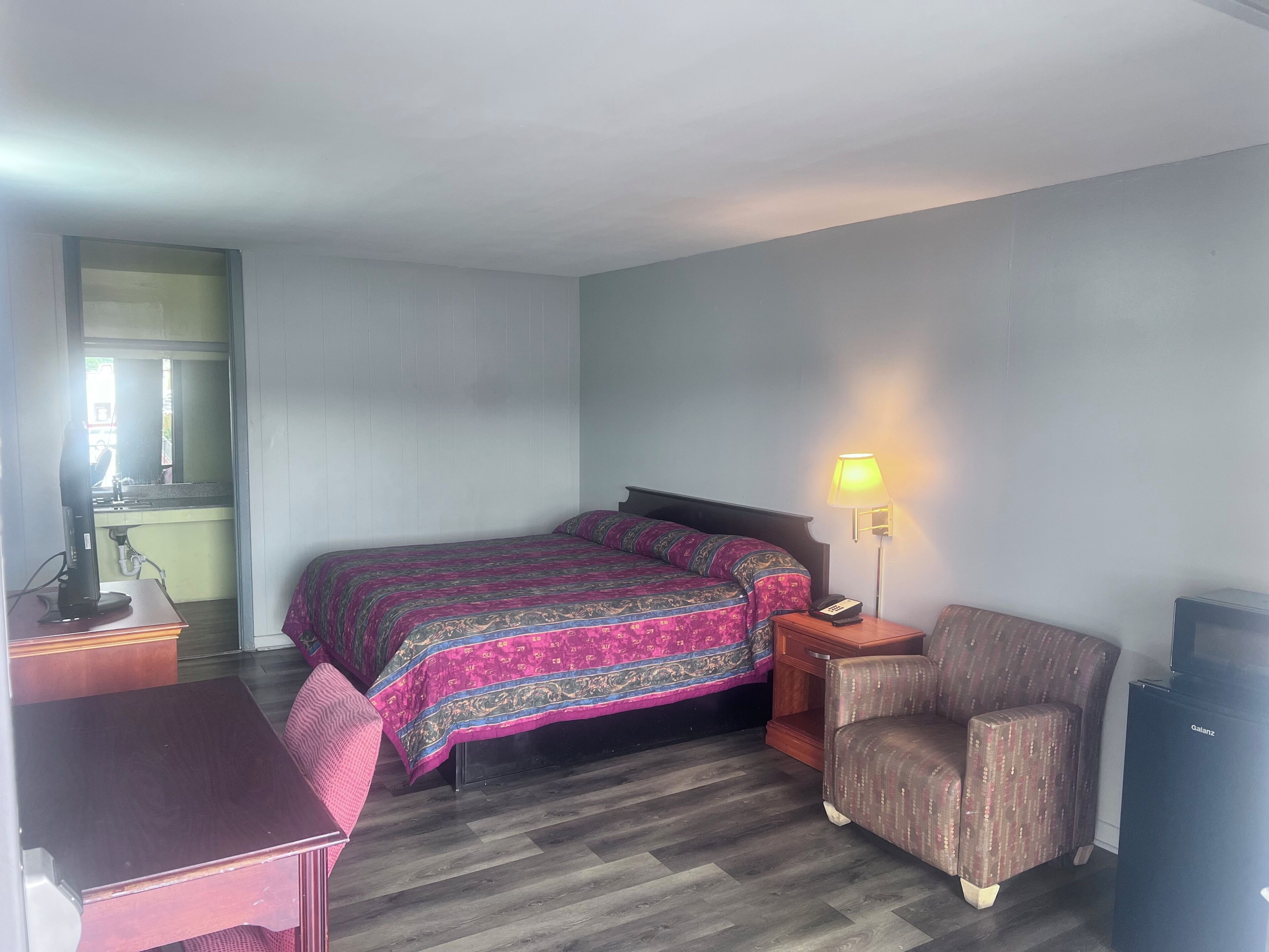 Un dormitorio con cama, mesita de noche, lámpara, sillón y escritorio.