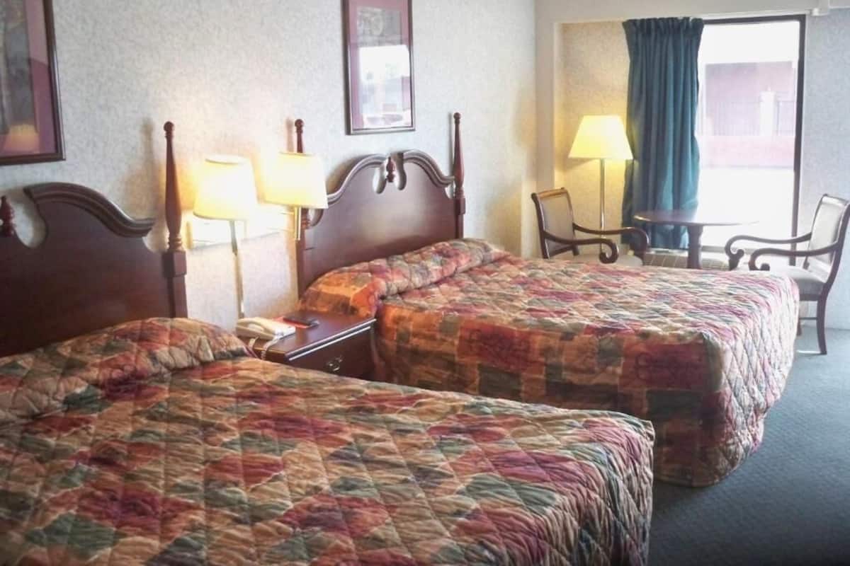 Et hotelværelse med to senge, en stol, et bord og et vindue med gardiner.
