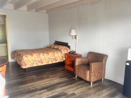 A hotel room with a bed, a chair, a nightstand, and a lamp.
