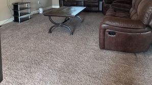 Una sala de estar con ventilador de techo, un televisor de pantalla plana montado en la pared, un sofá de cuero marrón, un sillón reclinable marrón y una pequeña mesa de centro.
