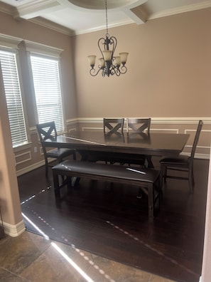 A dining room with a dark wooden table, benches, and chairs, a chandelier, and large windows with blinds. - Charming en-suite bedroom in Houston with all bill included. (Houston)