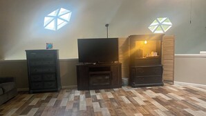 A living room with a flat-screen TV, wooden cabinets, and a herringbone-patterned floor. - Welcome to the Round Roost- 3 story+sleeps 16+Lake Ham+grill+decks+game room (Hot Springs)