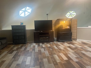 A living room with a flat-screen TV, wooden cabinets, and a herringbone-patterned floor. - Welcome to the Round Roost- 3 story+sleeps 16+Lake Ham+grill+decks+game room (Hot Springs)
