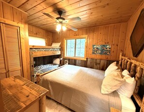 Ein Holzhütten-Schlafzimmer mit Etagenbetten, Deckenventilator, Fenster und Holztisch.