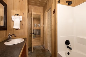 A wooden bathroom with a sink, mirror, towel rack, shower, and a door leading to a hallway with framed pictures. - Mountain Cabin Near Yellowstone with Scenic Views, West Yellowstone, Montana (West Yellowstone)