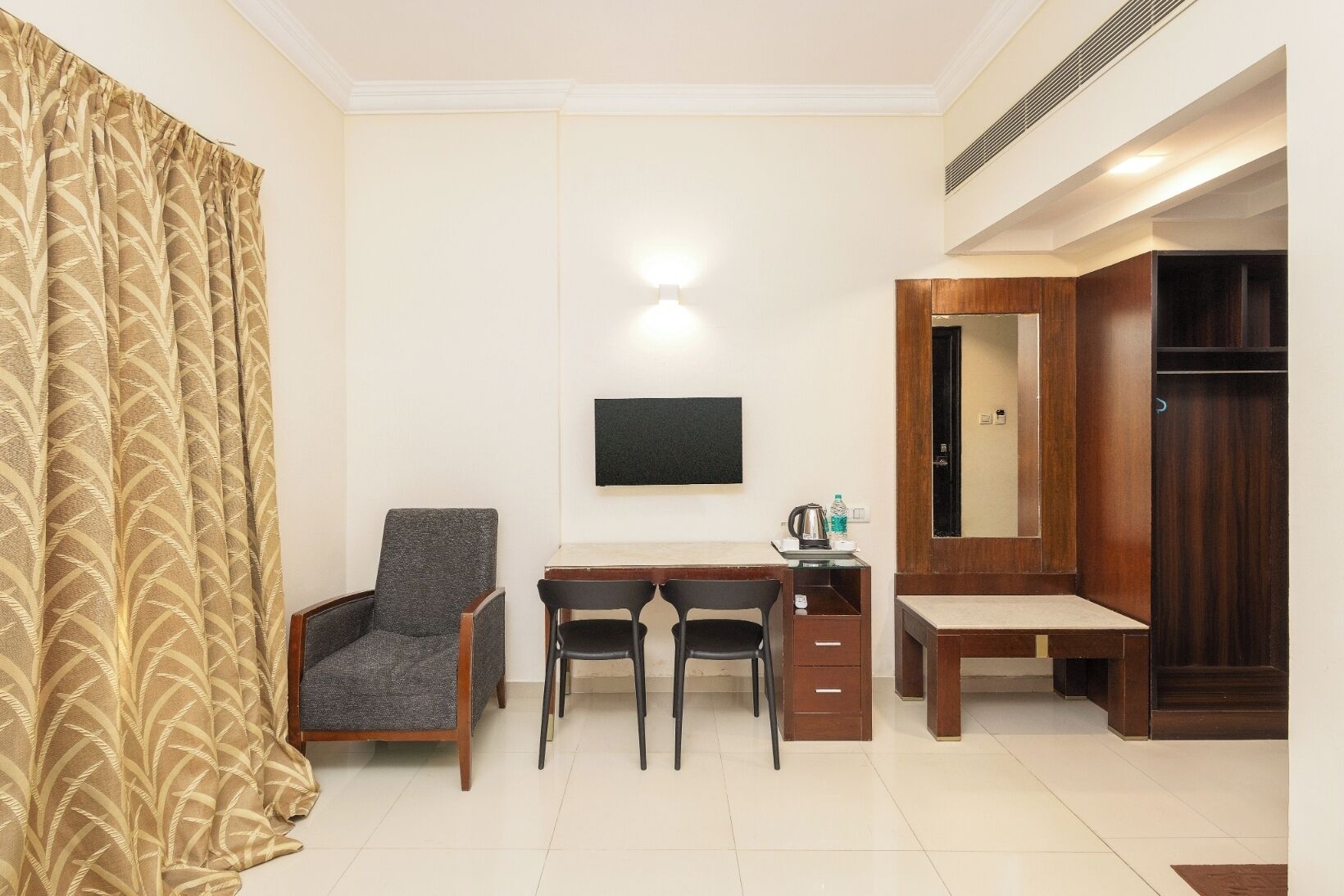 Habitación de hotel con escritorio, dos sillas, televisión, armario y espejo.