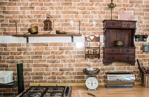A kitchen with a brick wall, a gas stove, a scale, and wooden cabinets. - The Sicilian Farmhouse (Palmeri - Ferrante)