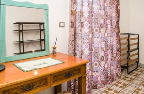 A room with a wooden desk, a mirror, a patterned curtain, and a metal rack. - The Sicilian Farmhouse (Palmeri - Ferrante)
