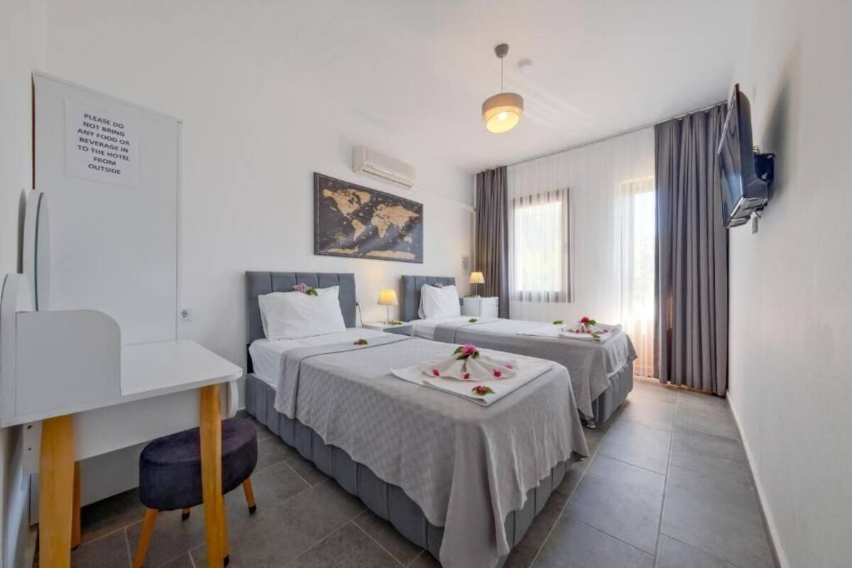 Habitación de hotel con dos camas, un escritorio, una silla, un mapa en la pared y un televisor montado en la pared.