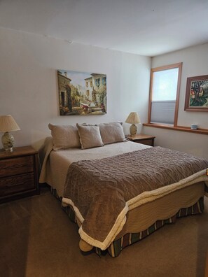 Ein Schlafzimmer mit einem großen Bett, zwei Nachttischen, einem Fenster mit Jalousien und zwei Wandlampen.