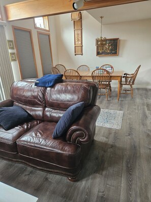 Eine braune Ledersofa mit zwei Kissen, ein Holzesstisch mit Stühlen und eine Pendelleuchte.