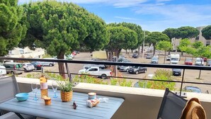 A balcony with a table set for dining, chairs, a potted plant, and a straw hat on a chair. - Près du Rivage Méridien (Le Grau-du-Roi)