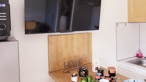 A kitchen with a flat-screen TV, wooden bar stools, a sink, and various kitchen items on the counter. - Près du Rivage Méridien (Le Grau-du-Roi)