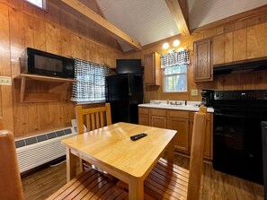 Ein Holzhütten-Interieur mit einem Esstisch, Stühlen, einer Mikrowelle, einem Kühlschrank, einem Herd und einem Spülbecken.