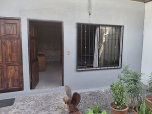Ein Gebäude mit Holztür, offener Innentür, vergittertem Fenster und Topfpflanzen.