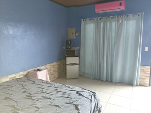 Ein Schlafzimmer mit einem Bett, einem kleinen Tisch, einem Kühlschrank und einem Fenster mit Vorhängen.