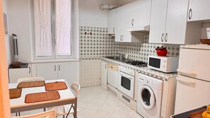 A compact kitchen with white cabinets, a stove, a microwave, and a washing machine.