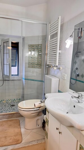 A bathroom with a toilet, sink, shower, and a glass-enclosed shower area.