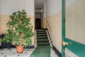 Un corridoio con una pianta in vaso, una scala con tappeto verde e una porta con maniglia in ottone.