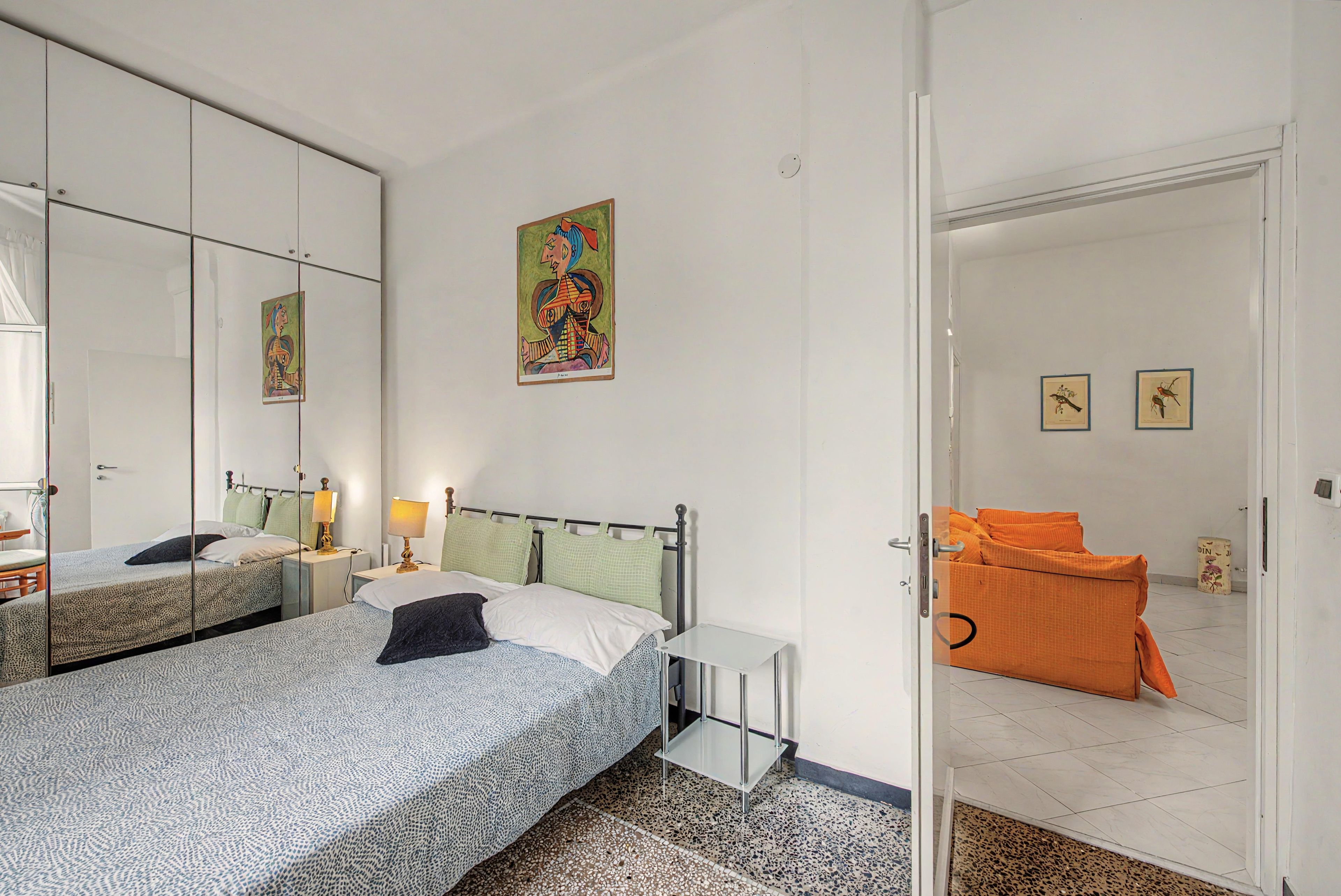 Une chambre d’hôtel avec deux lits, un grand miroir, un tableau et une porte donnant sur une autre pièce.