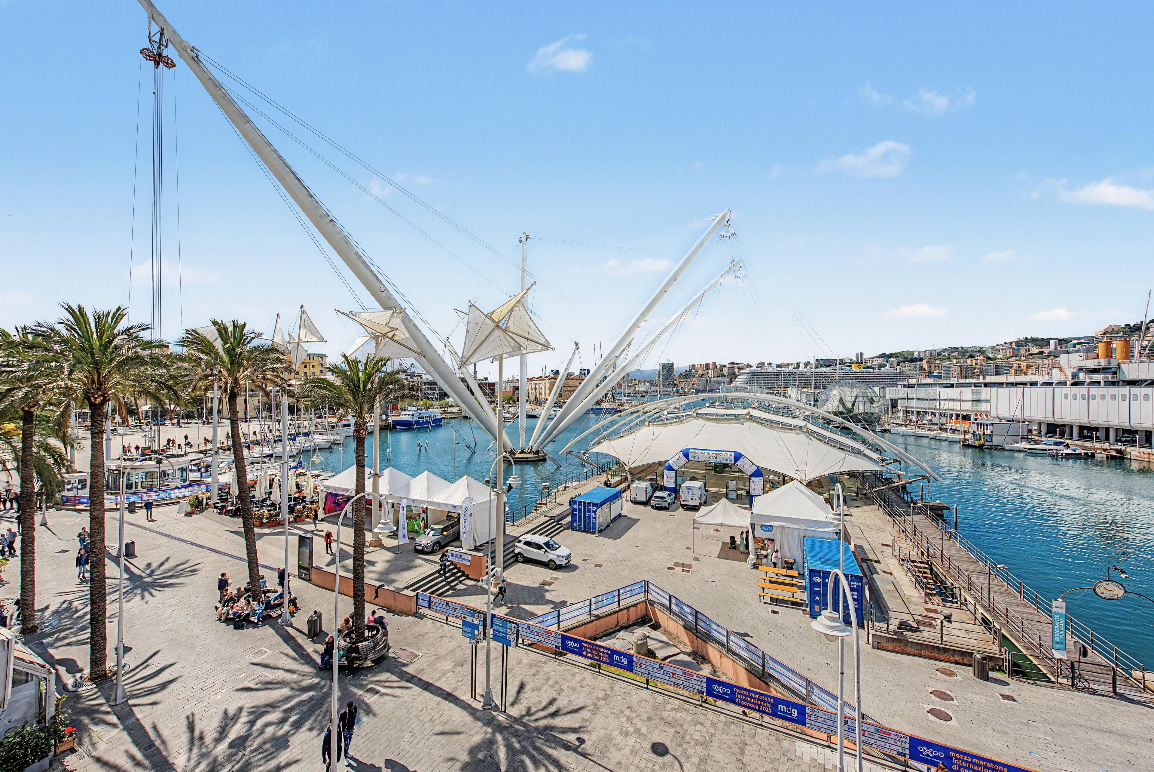 A marina with boats, a pedestrian walkway, and a large white structure.