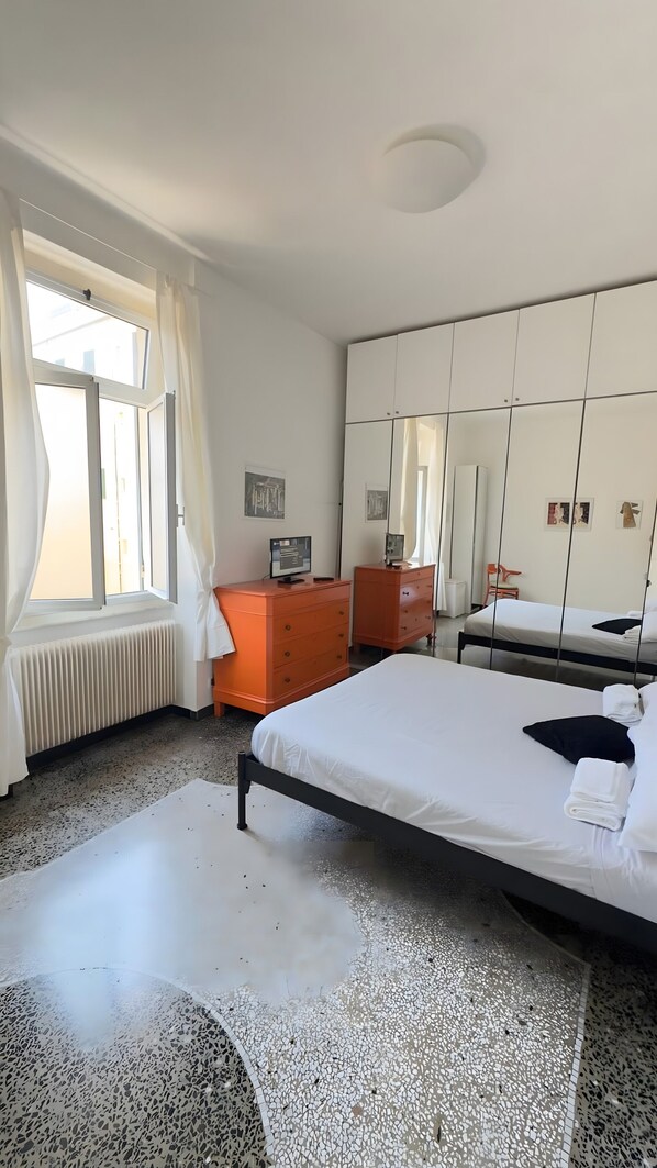 A bedroom with a bed, a dresser, a radiator, a window with curtains, and a mirror.