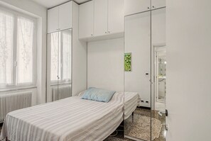 A bedroom with a bed, a radiator, a window with curtains, and a door leading to a bathroom.
