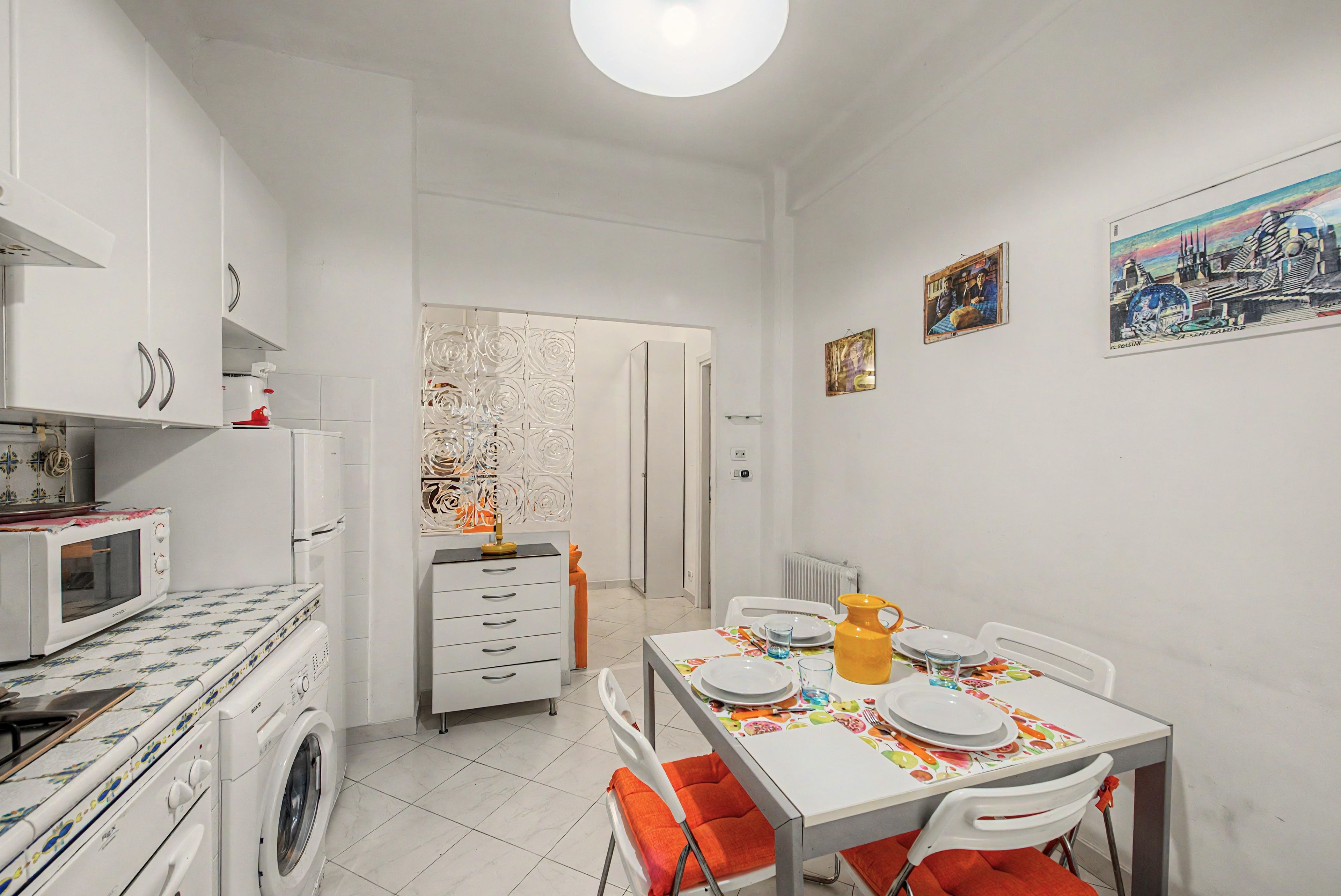Une cuisine compacte équipée d’un four à micro-ondes, d’un lave-linge et d’un coin repas avec une table pour deux personnes.