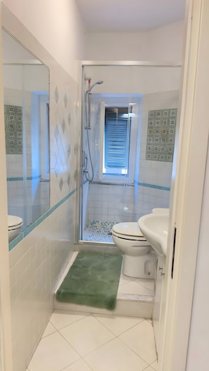 Ein kleines Badezimmer mit Toilette, Dusche und einer grünen Matte.
