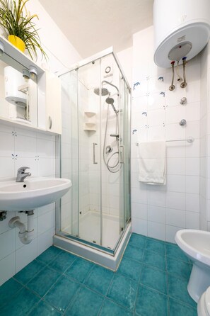 Un baño con ducha envuelta en vidrio, un lavabo, un inodoro y suelo de baldosas blancas.