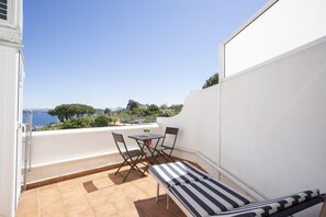 A balcony with a table and chairs, a striped lounge chair, and a view of the sea and greenery. - Ischia Apartment with seaview terrace for 4 people (ISCHIA)