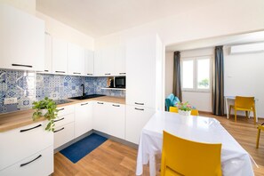 A modern kitchen with white cabinets, a blue and white tiled backsplash, a microwave, and a dining area with a table and chairs. - Ischia Apartment with seaview terrace for 4 people (ISCHIA)