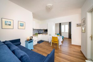 Una sala moderna con un sofá azul, una mesa de comedor con sillas amarillas, una cocina con armarios blancos y cuadros en las paredes.