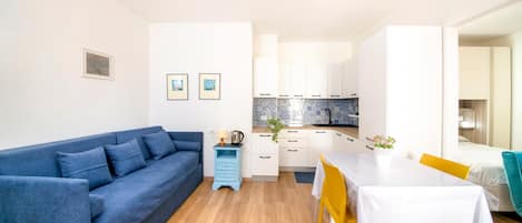 A compact living space with a sofa, a dining table, a kitchen area, and a small side table.