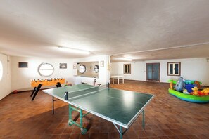 Une pièce équipée d’une table de ping-pong, d’un baby-foot et d’une petite piscine gonflable avec des jouets.